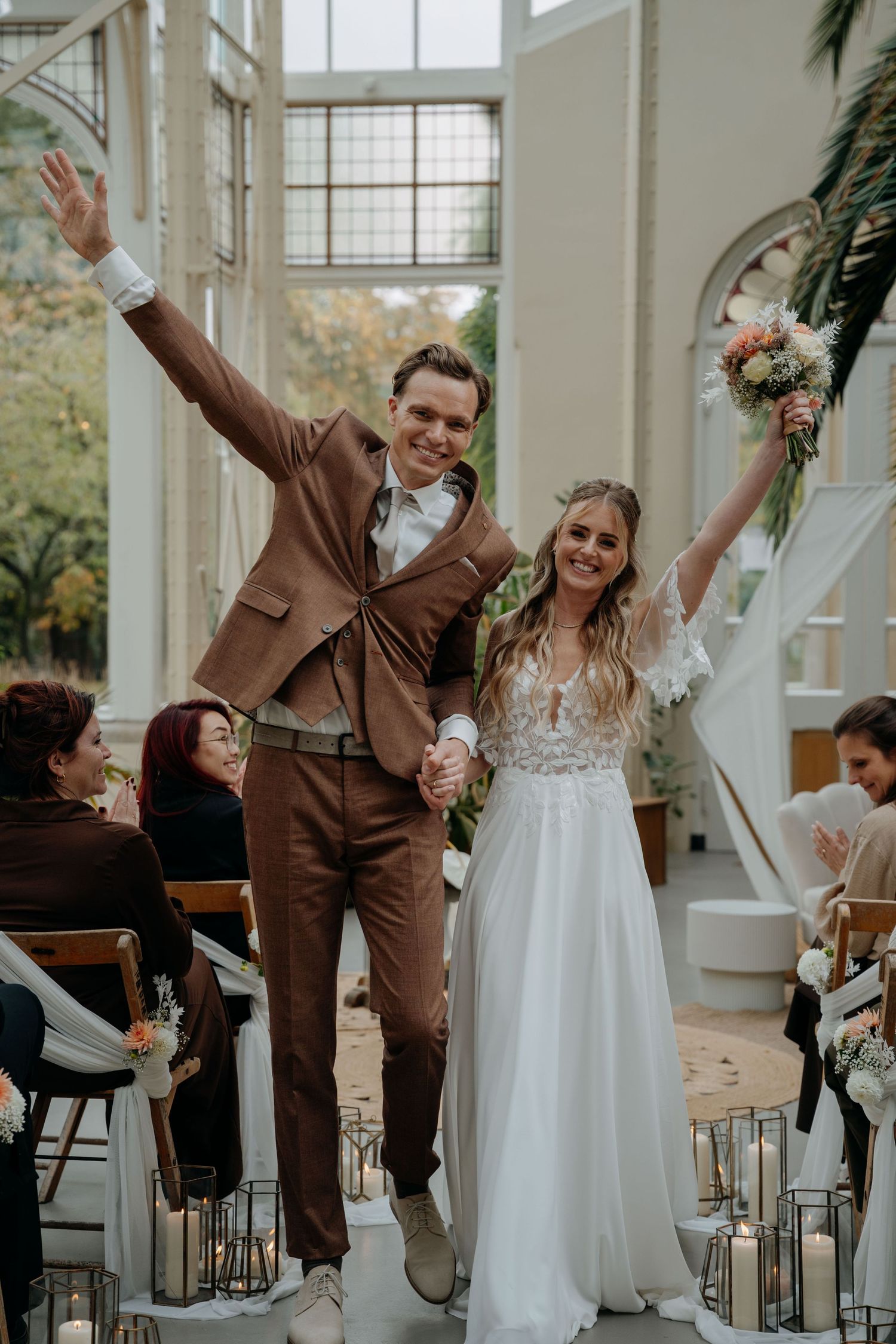 Joyful couple celebrates during wedding ceremony in bright indoor venue with large windows and natural lighting.