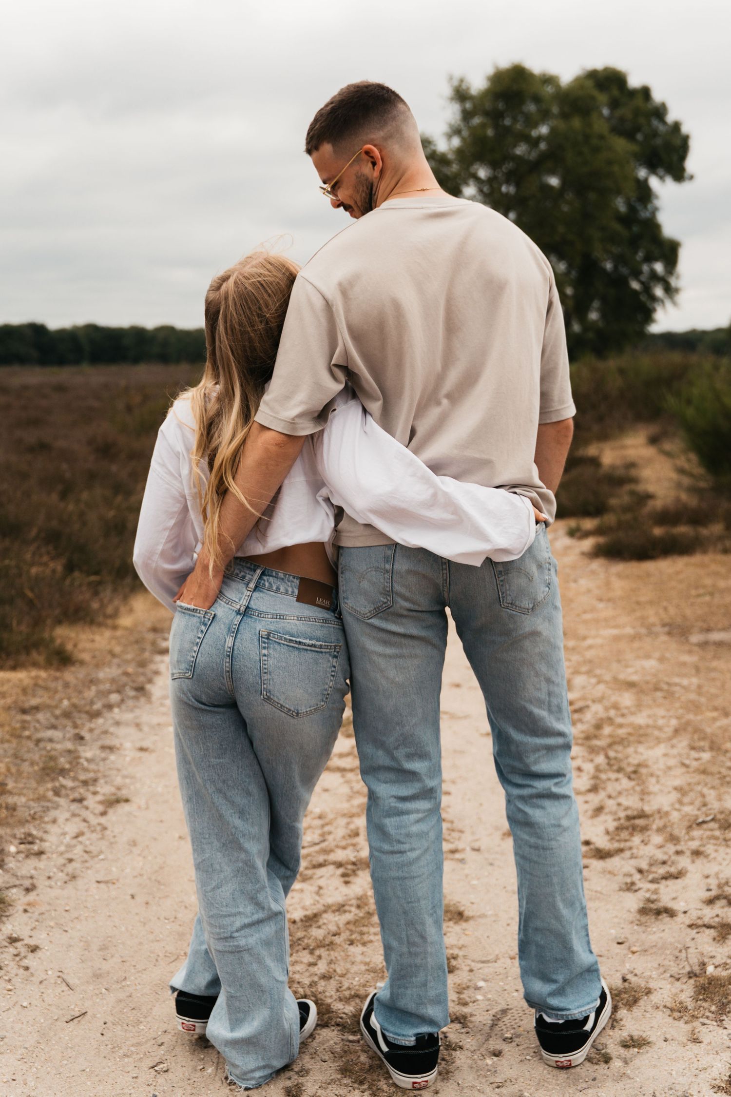 Een verliefd stel in matching jeans wandelt samen over een zandpad op de heide in Laren.