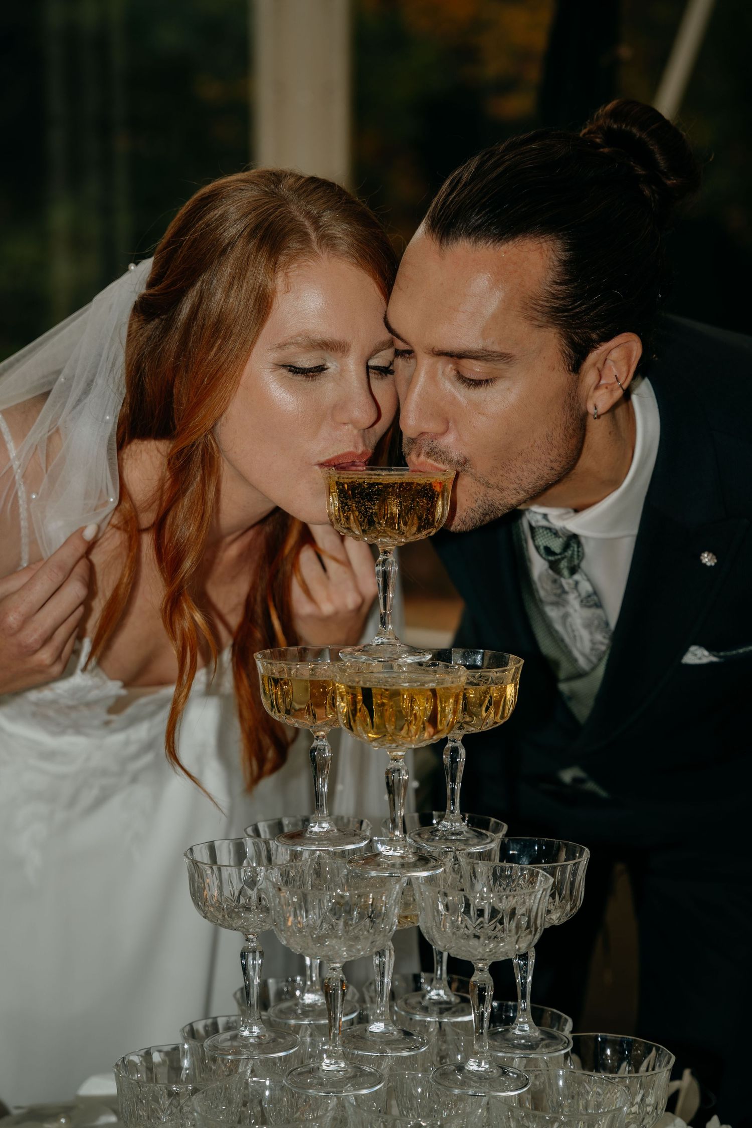 Bride and groom sipping champagne together from a crystal coupe atop an elegant champagne tower at their wedding reception.