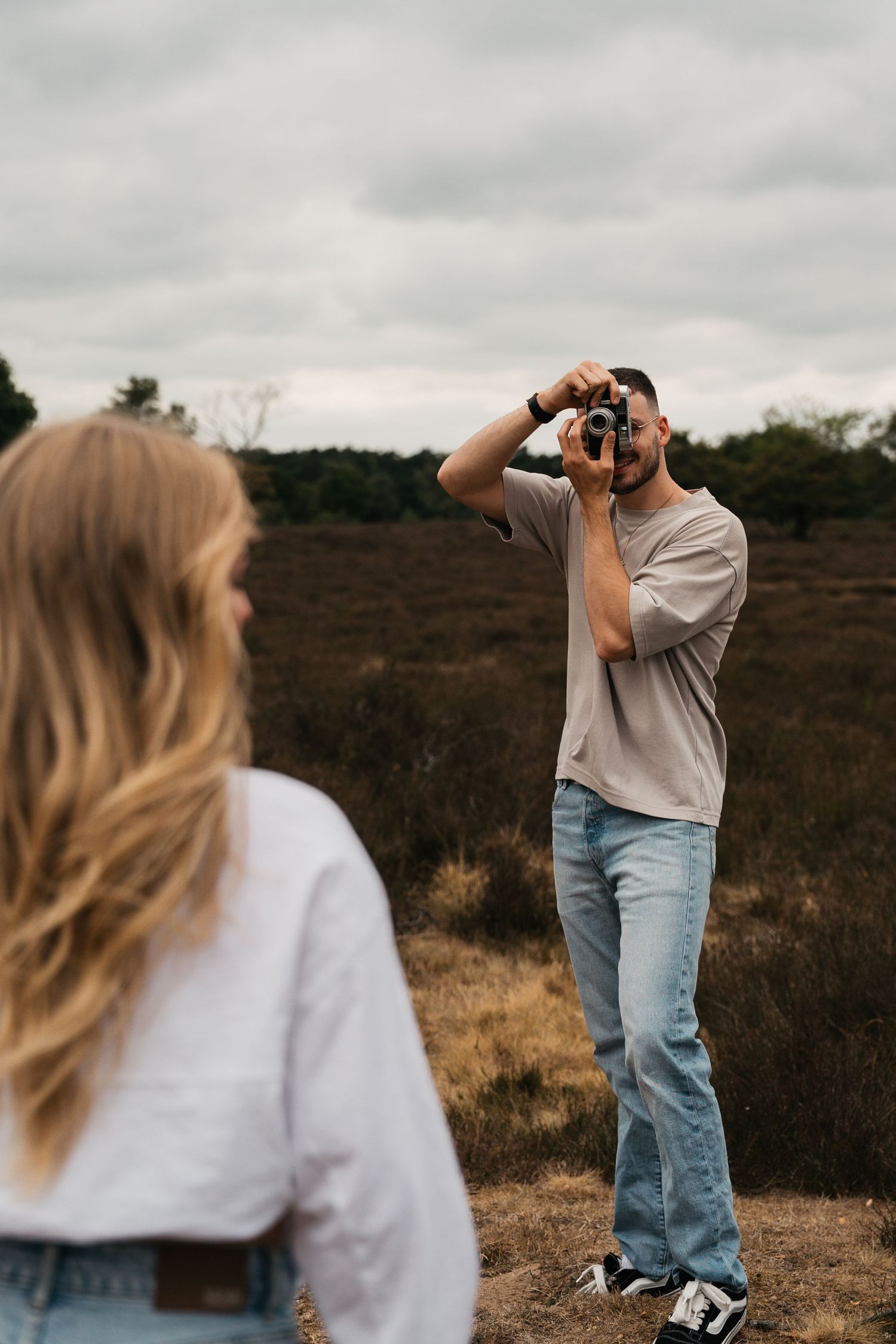Een verliefd stel dat elkaar fotografeert op de paarse heide in Laren tijdens een frisse lentedag.