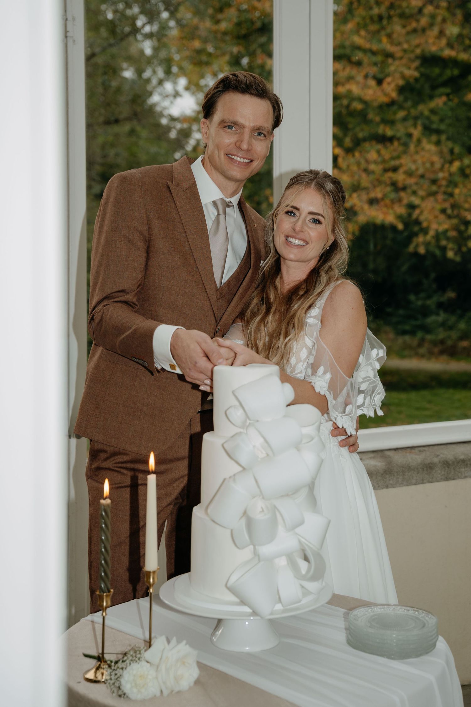 Wedding couple poses with their modern white geometric wedding cake and candlelit display.
