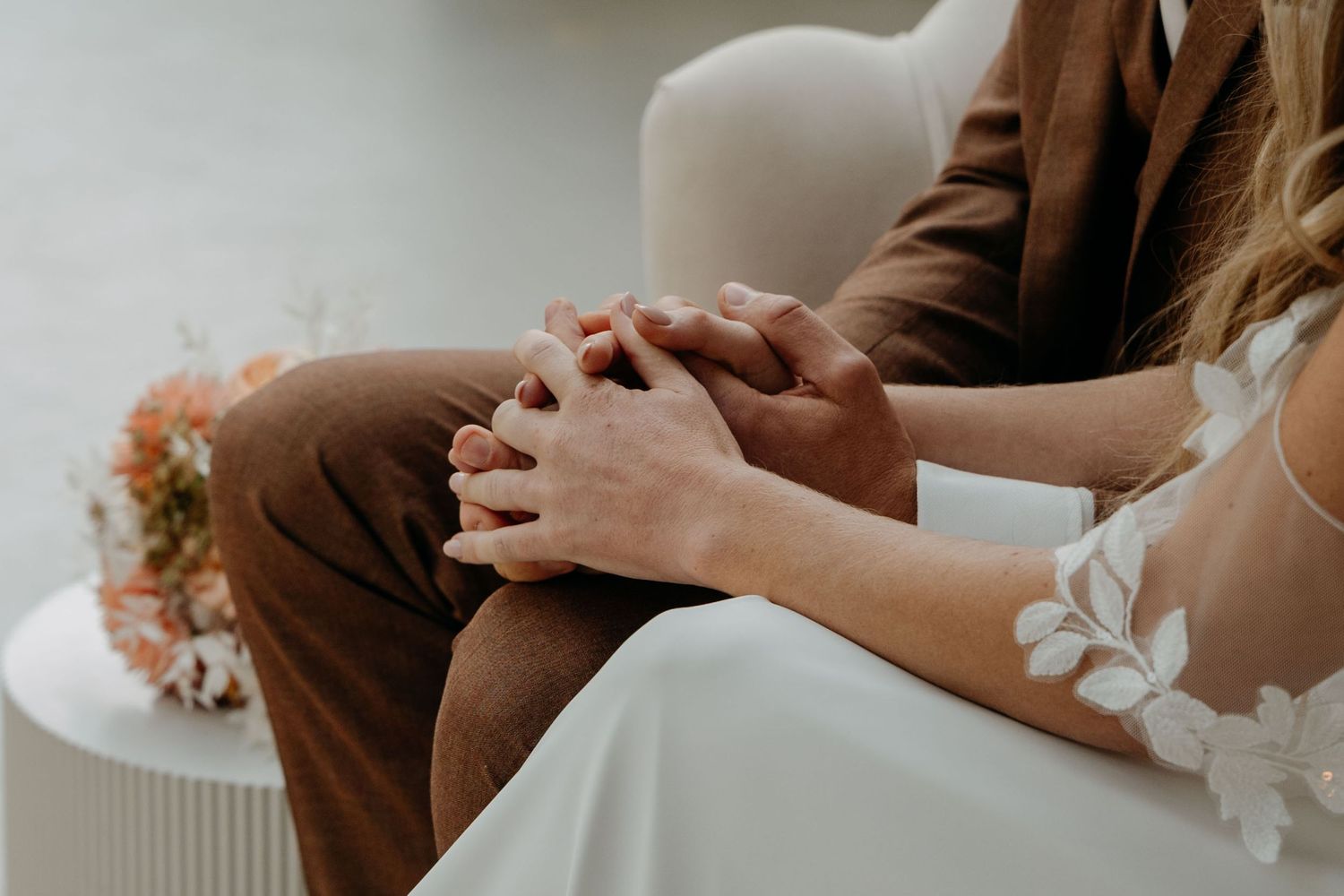 Two hands gently touch during an intimate moment against a soft neutral background.