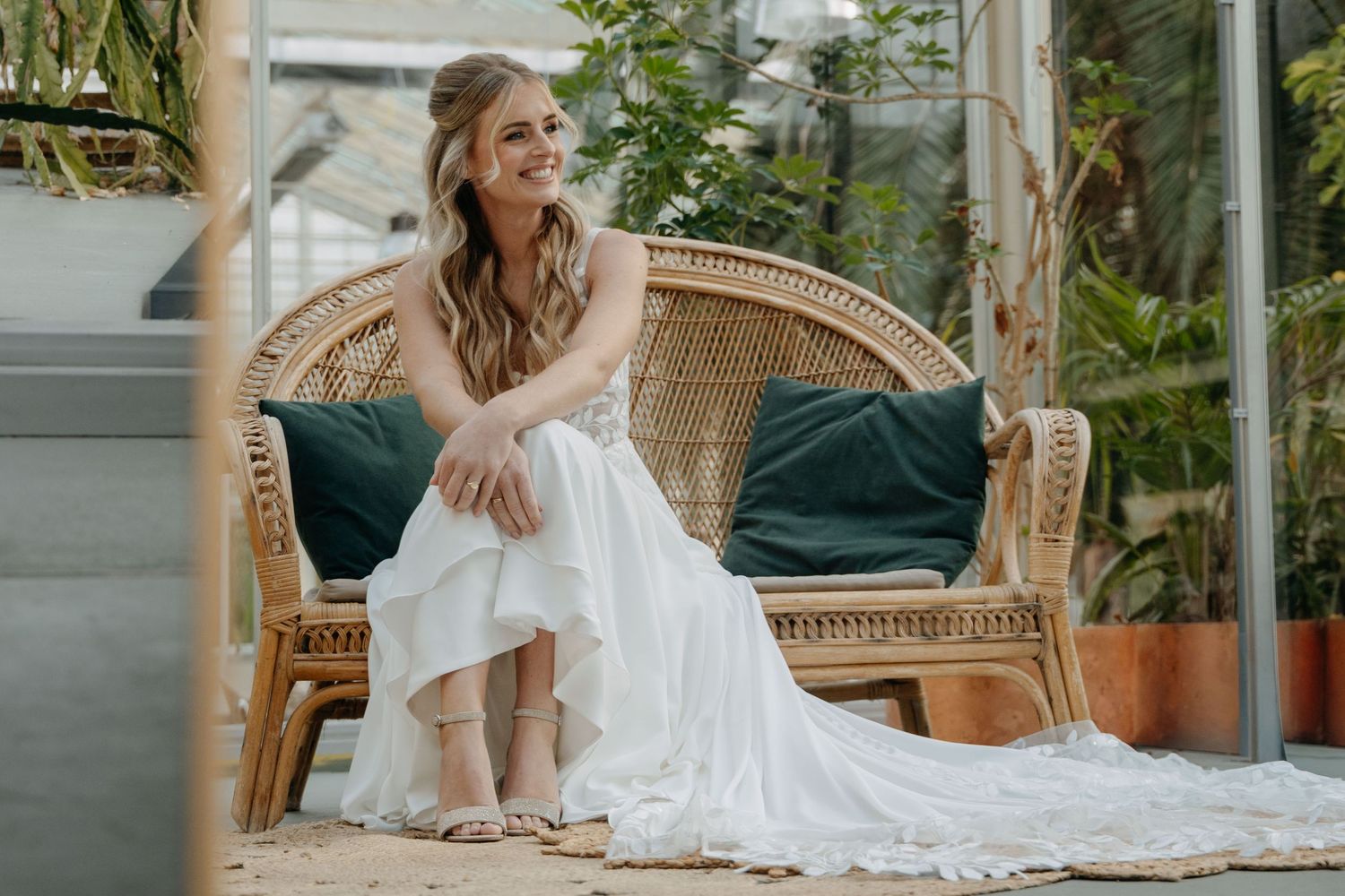 A bride in a flowing white dress lounges elegantly on a vintage wicker settee on a sunlit porch.