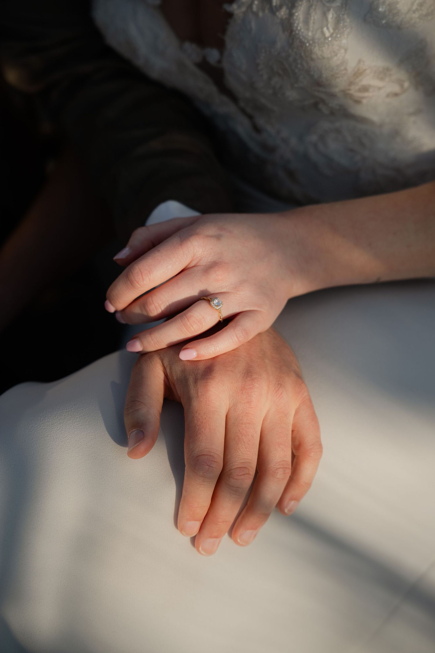 Bride and groom holding hands, showing engagement ring, wedding couple close-up shot with soft natural lighting.