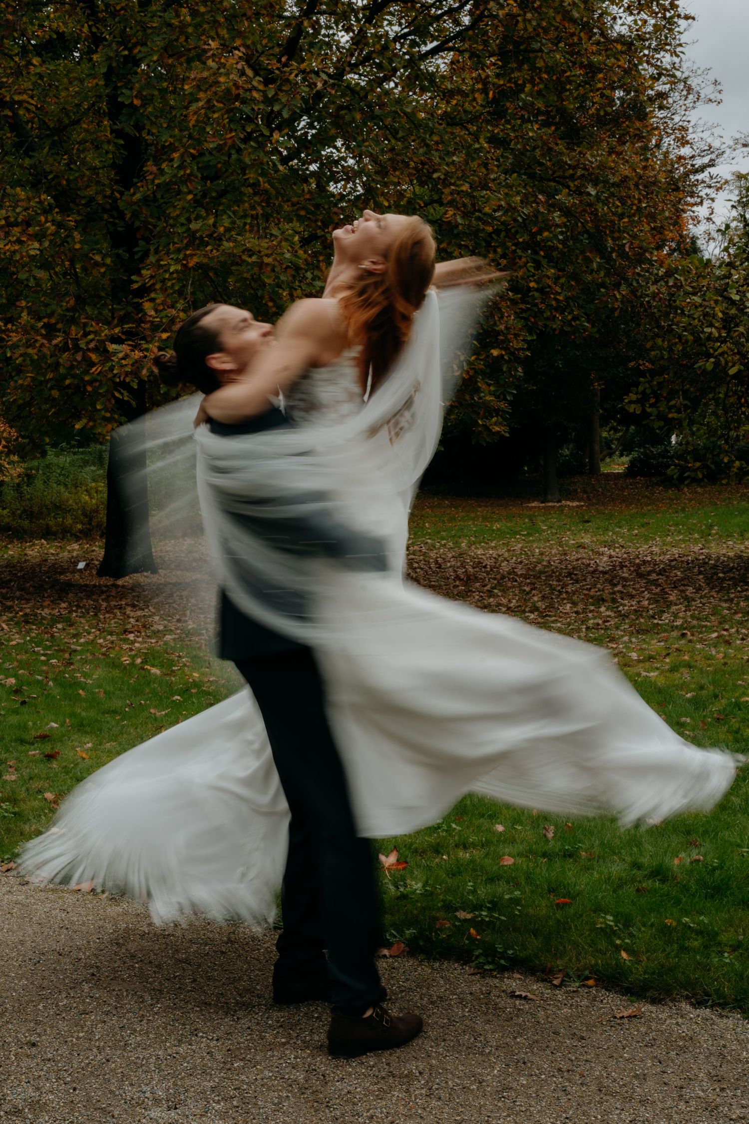 A couple dancing outdoors with the bride's white dress twirling in motion against an autumn backdrop.