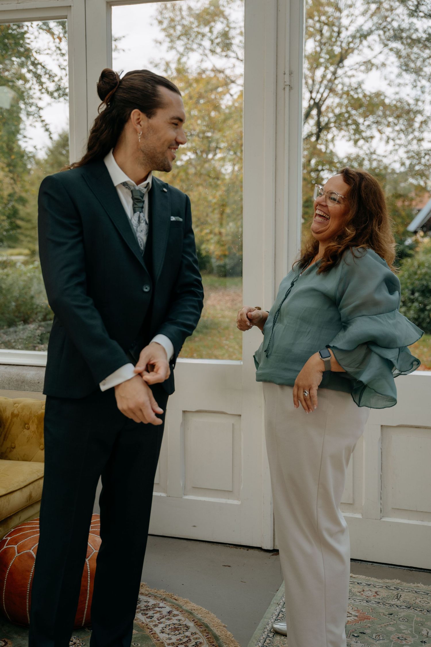 A man in a dark suit and a woman in a blue ruffled jacket share a joyful moment together indoors.