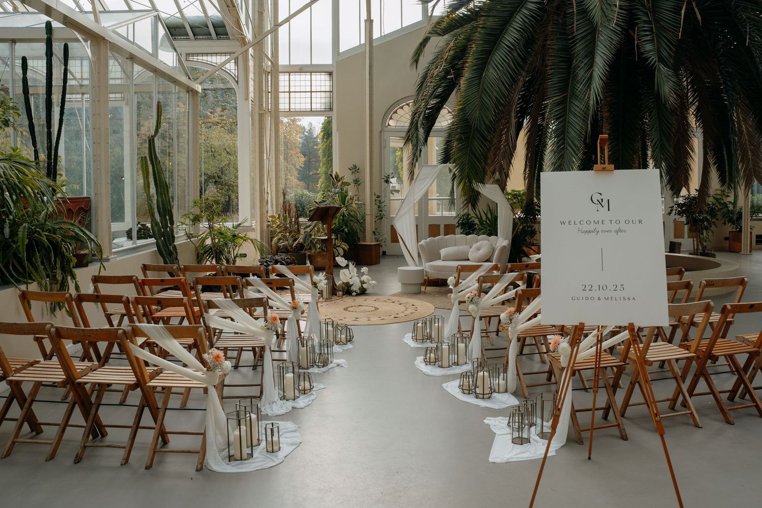 Interior view of a sunlit greenhouse conservatory with wooden folding chairs arranged in rows for an event.
