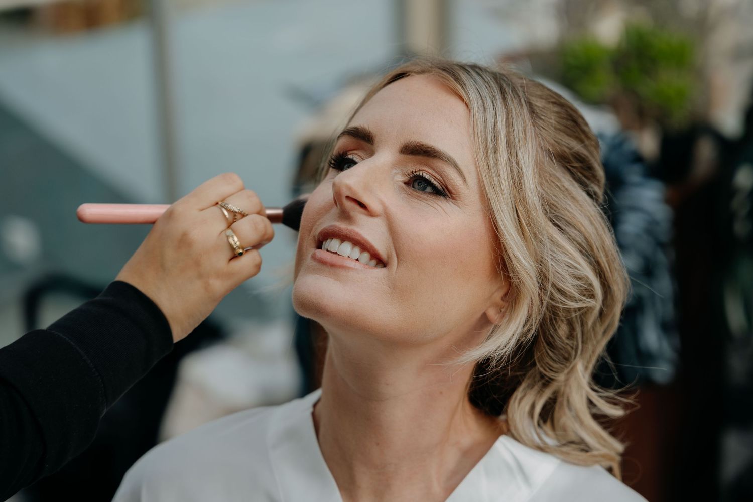 Makeup artist applies cosmetics to smiling client during professional beauty session in salon.
