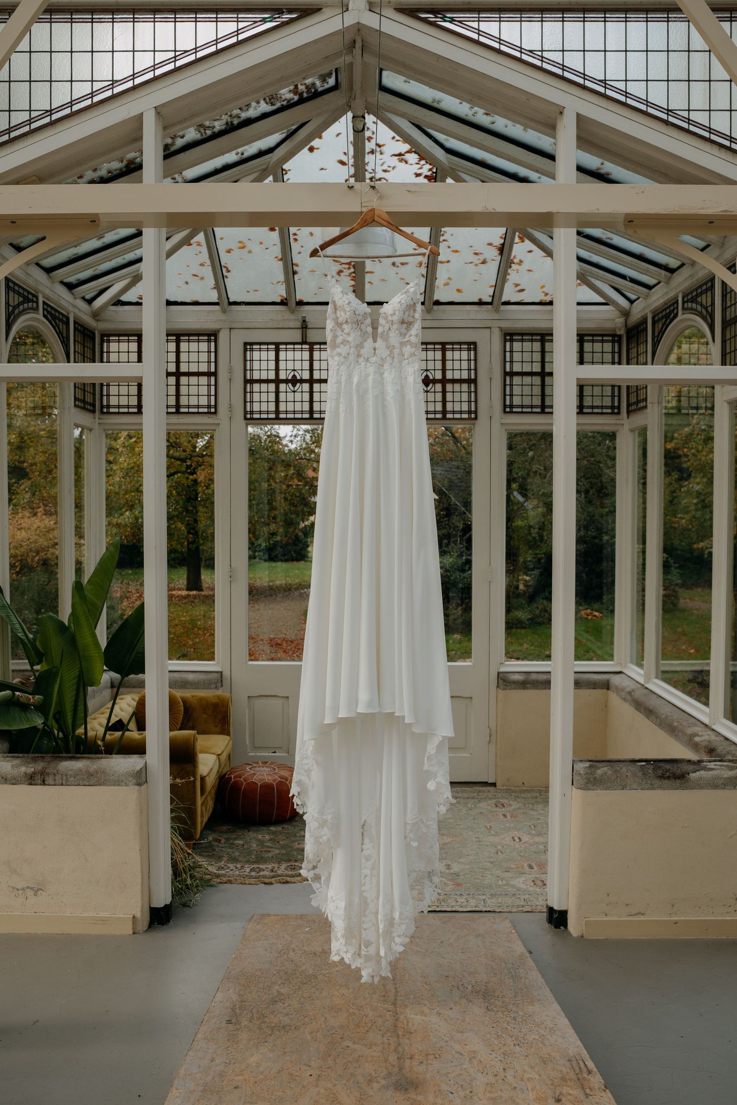 Wedding dress displayed in elegant glass conservatory with natural autumn scenery visible outside.