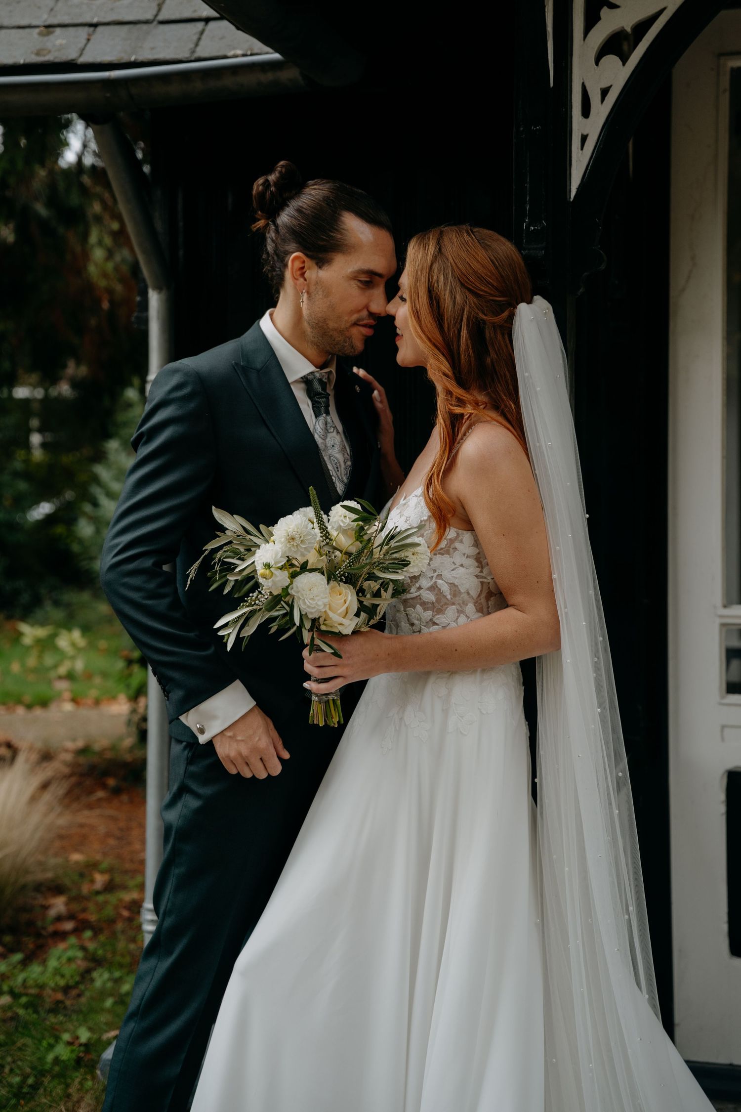 A tender moment between newlyweds with white floral bouquet against white columns.