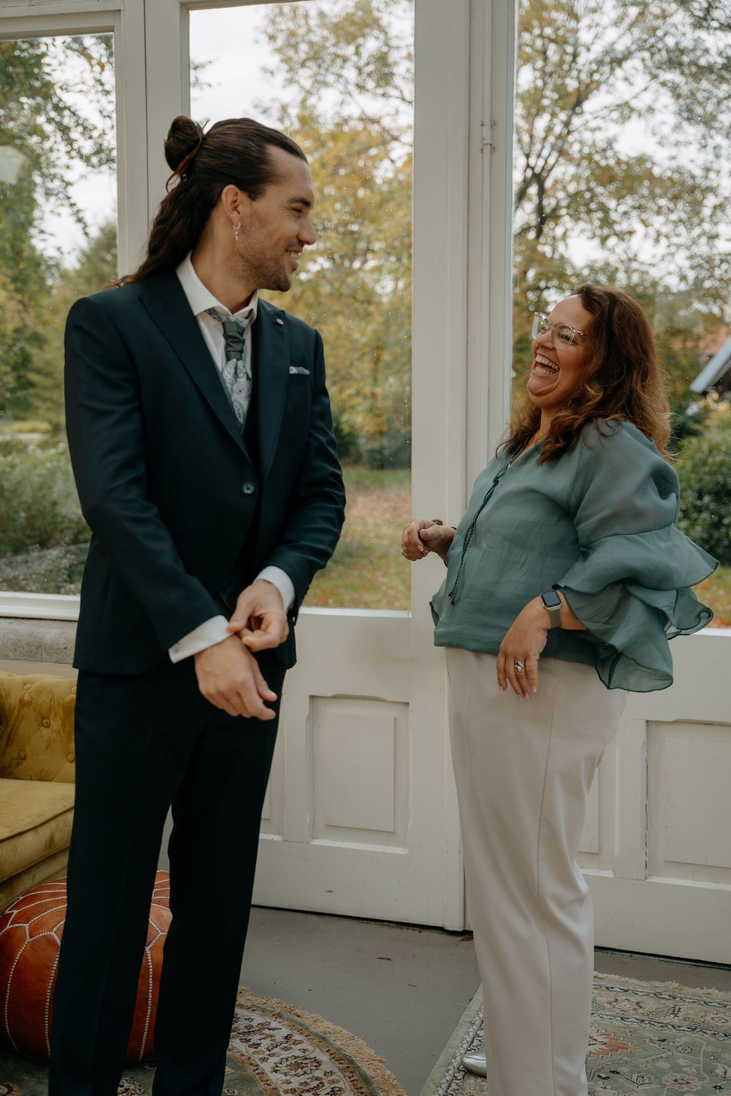 Couple sharing joyful moments and laughter on a sunlit porch during their wedding day.