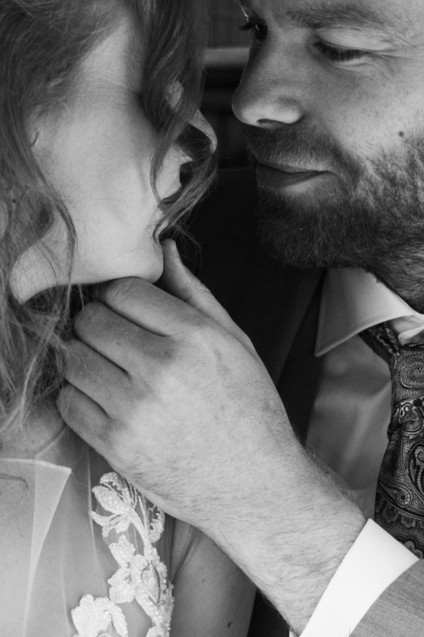 Black and white photo of a bearded groom tenderly holding brides face close to his during an intimate wedding moment.
