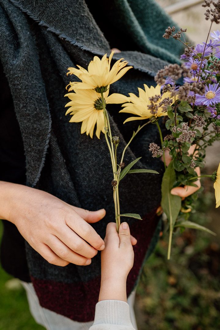 Kinderhand reicht Erwachsenenhand Blumen für einen Strauß