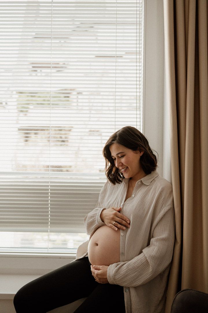 Schwangere sitzt auf Fensterbank beim Babybauchshooting