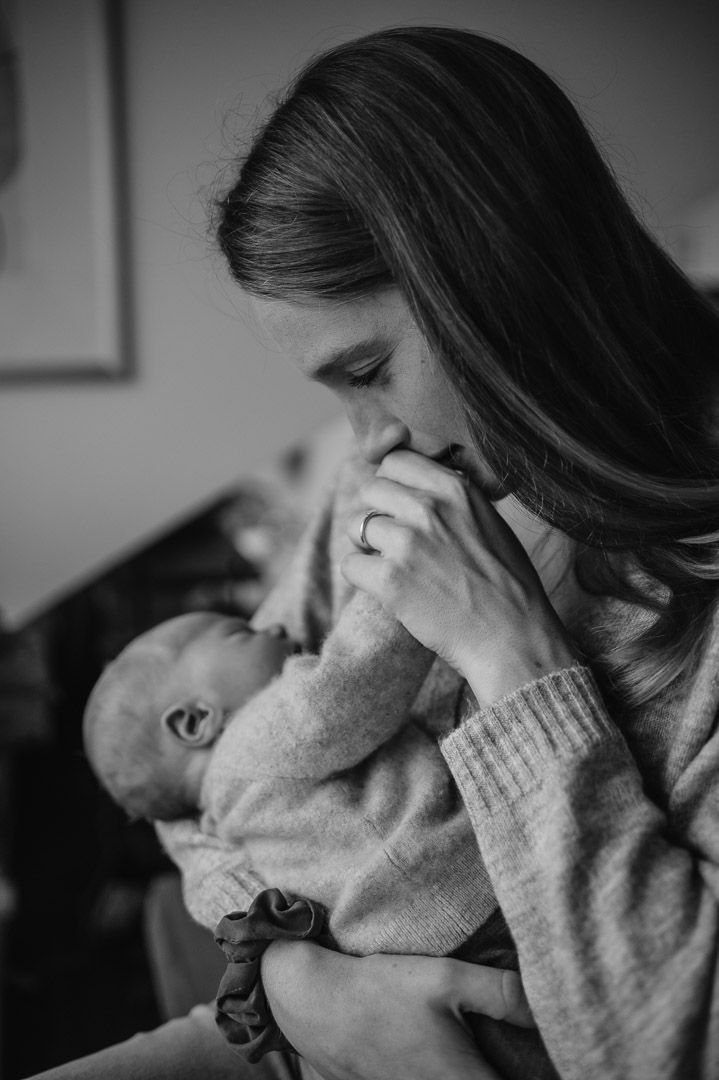 Mama hält Baby im Arm und küsst Händchen