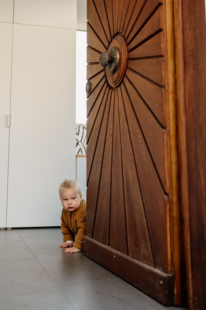 krabbelndes Baby schaut hinter einer Haustür hervor