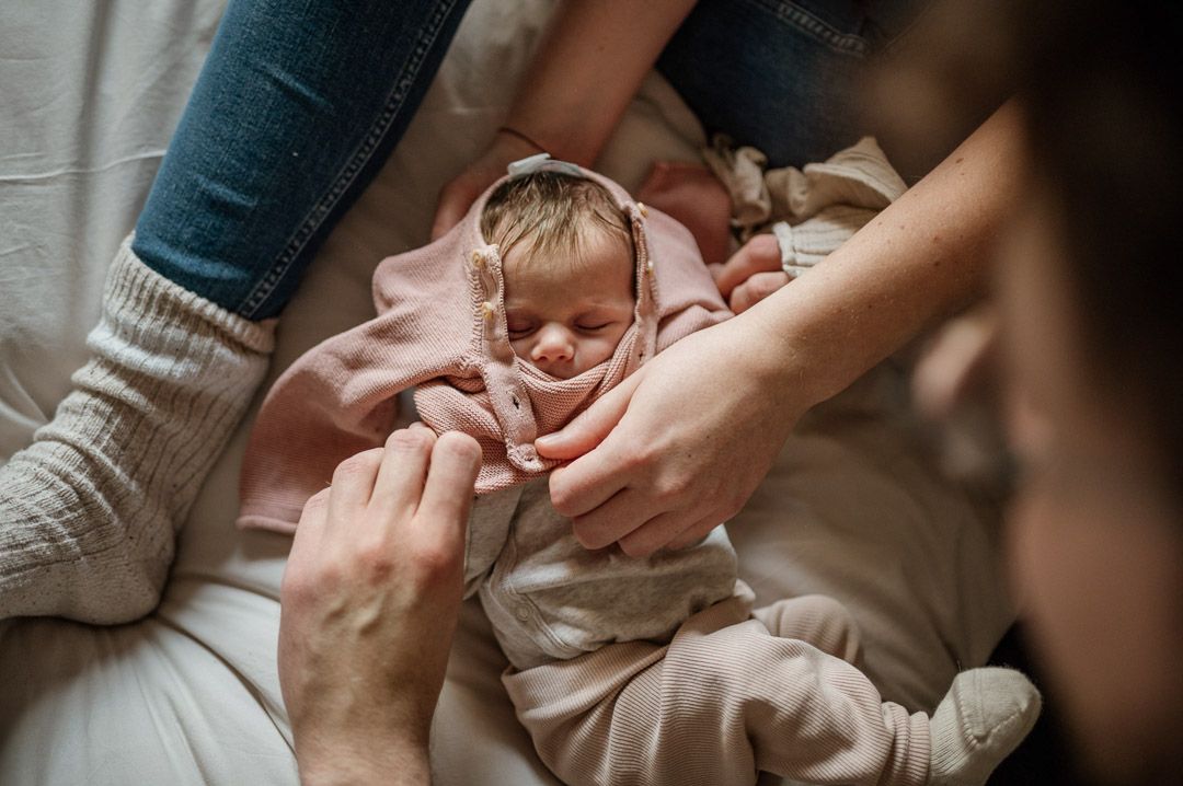 Baby wird von vier Händen ein Pullover angezogen
