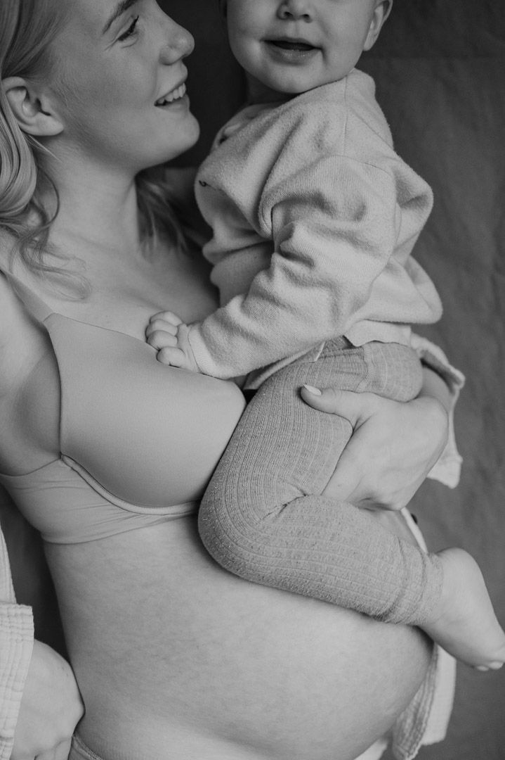 Kleinkind sitzt auf Babybauch seiner Mama