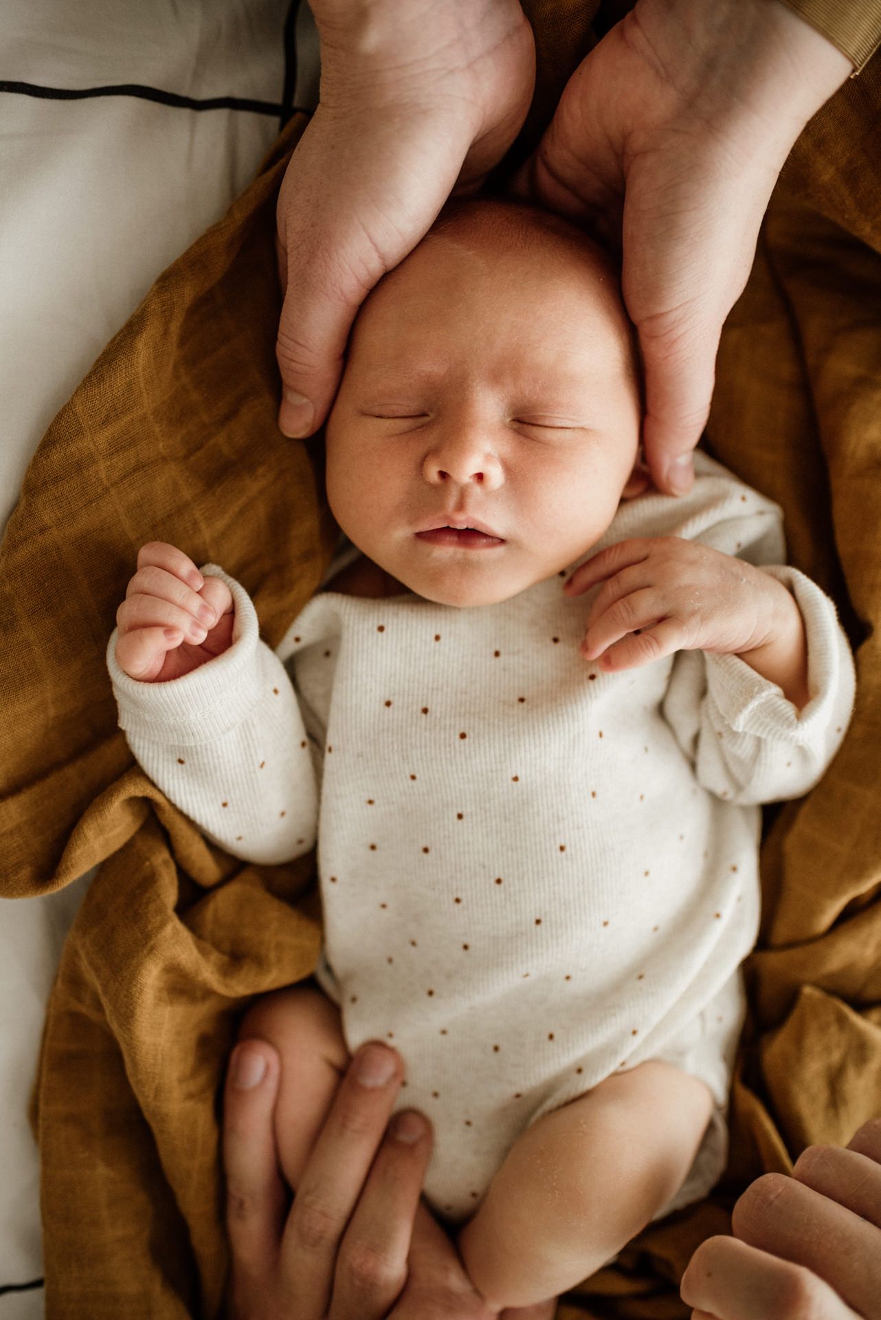 Baby liegt auf Bett und wird von Händen gehalten