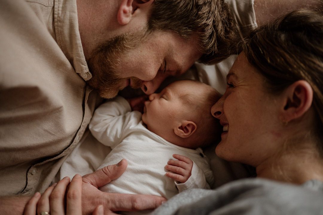 Eltern kuscheln mit Baby auf Bett