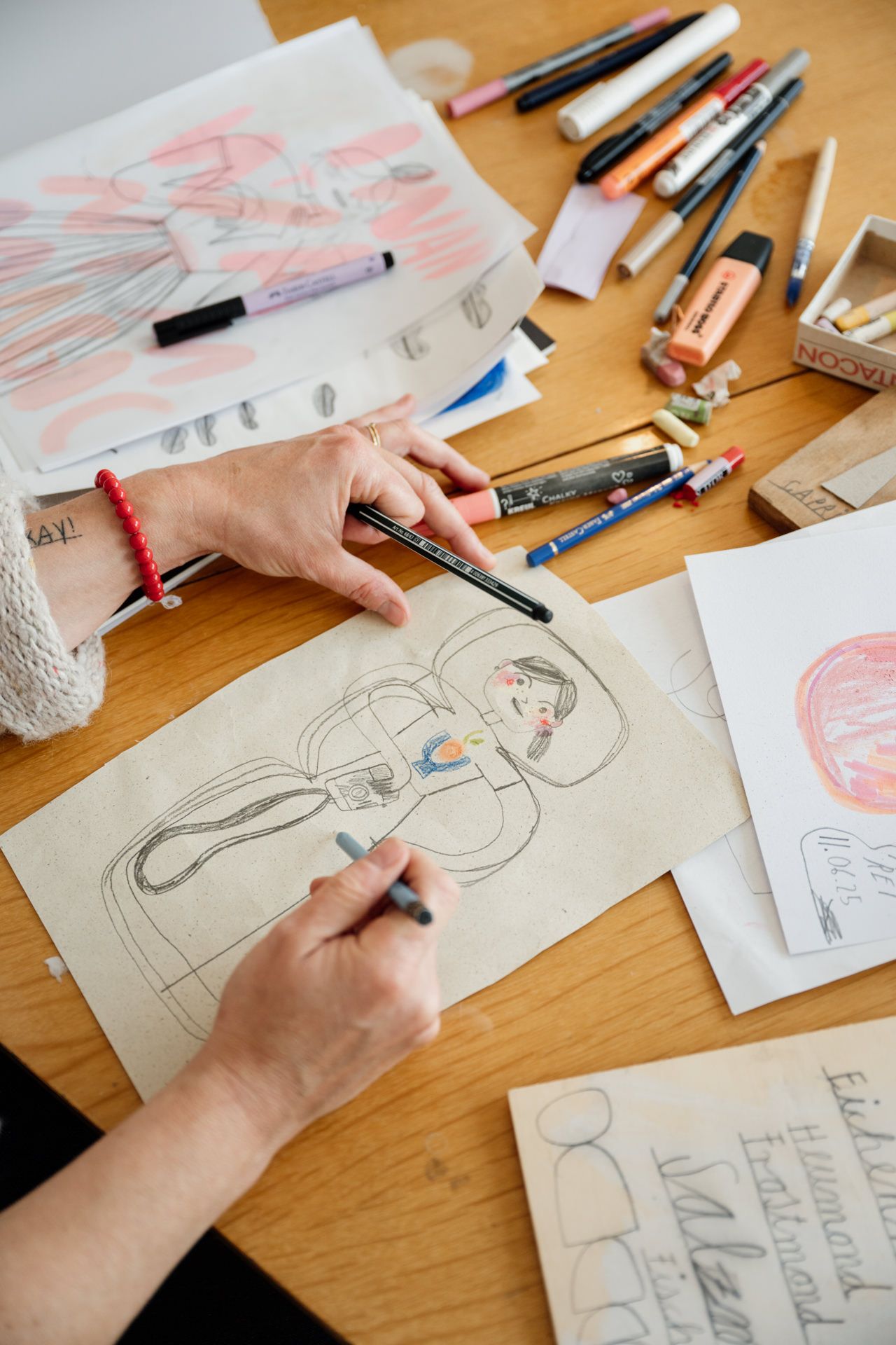 Hände zeichnen ein Bild auf einem Schreibtisch mit Malutensilien