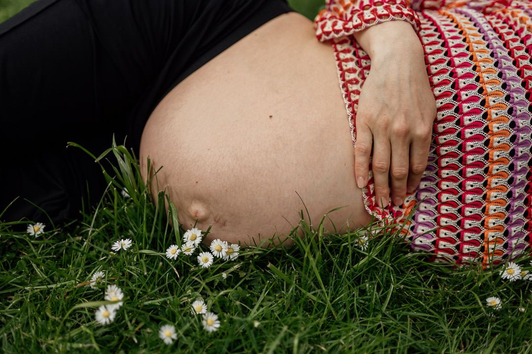 Babybauchshooting liegend auf Gänseblümchenwiese