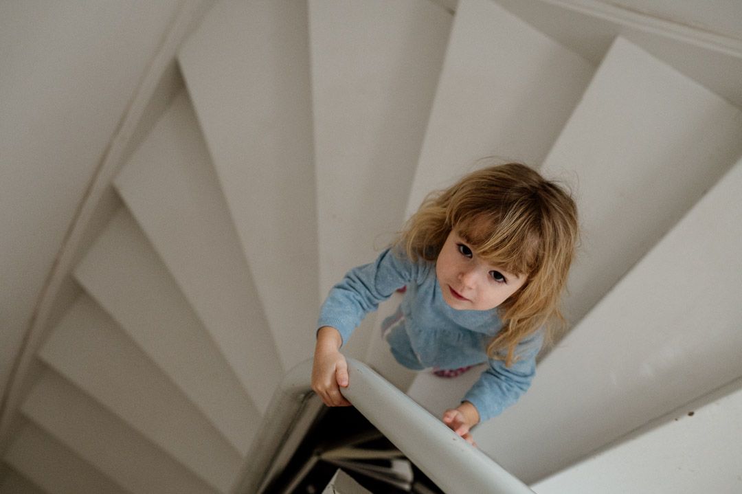 Kind in blauem Kleid steht auf weißer Wendeltreppe