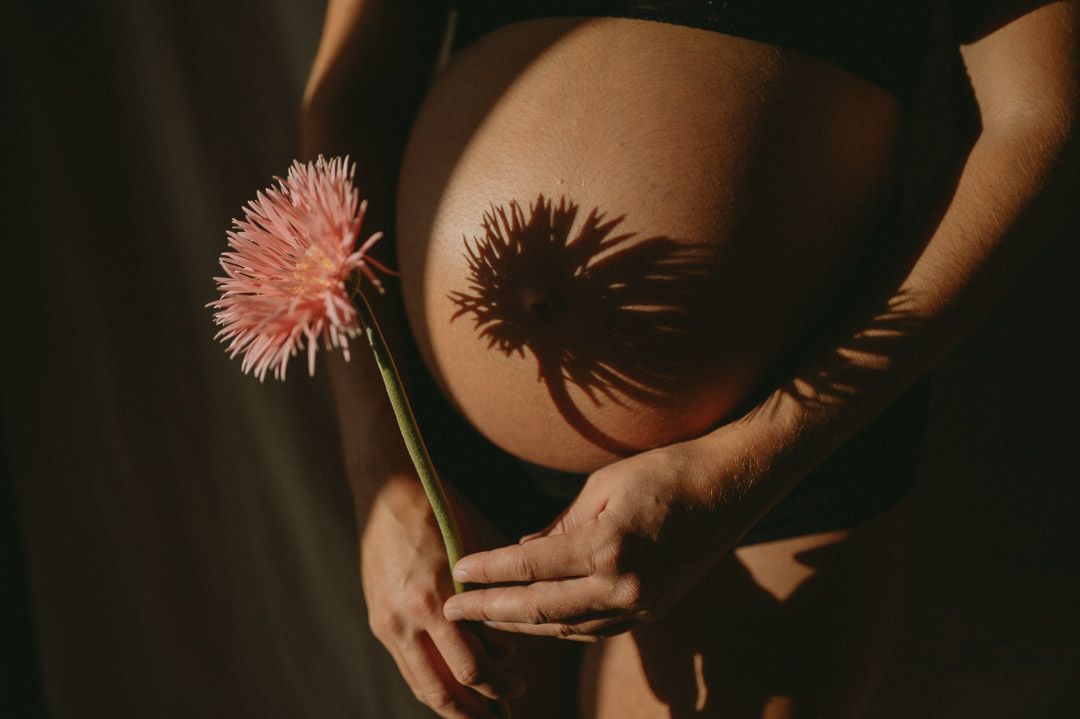 Schwangere hält eine Blume vor Babybauch mit Schatten