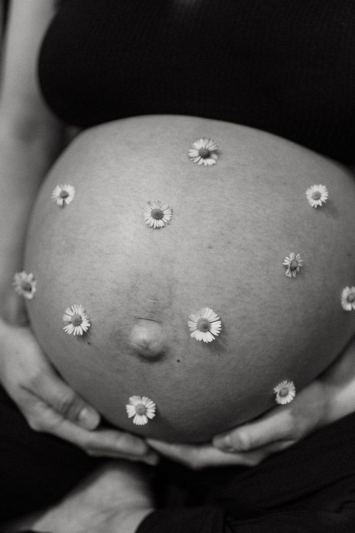 Babybauch dekoriert mit Gänseblümchen für Schwangerschaftsshooting
