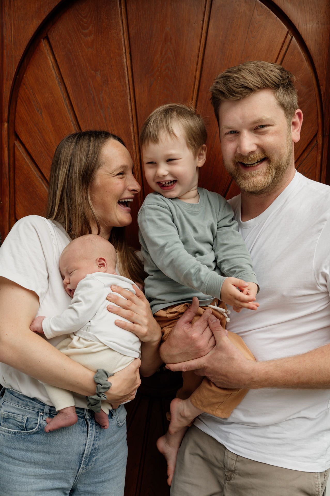 authentisches Familienportrait mit Kindern auf dem Arm vor Haustür