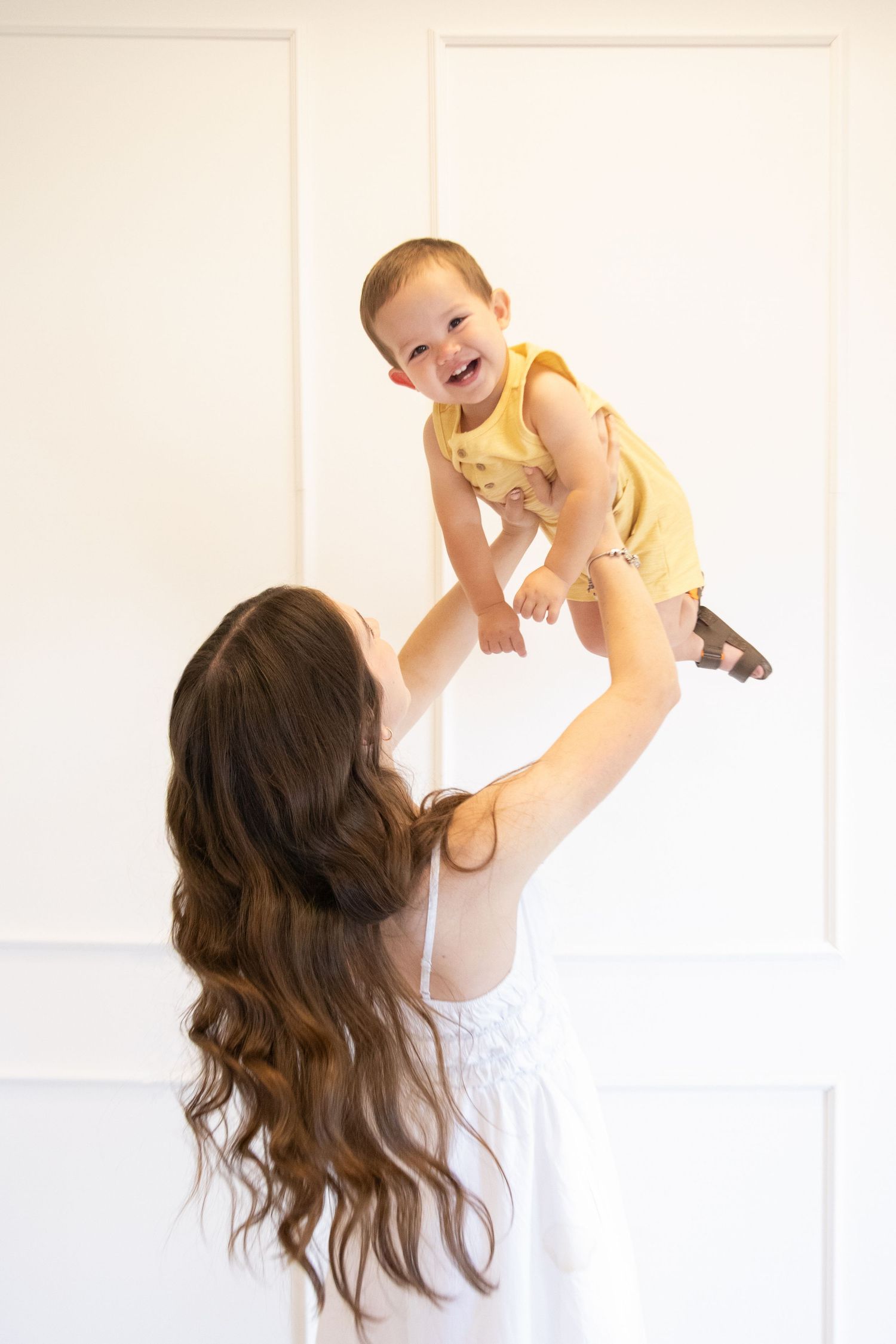 Mother holding her baby lifted up in a soft studio setting, captured in a warm motherhood moment.