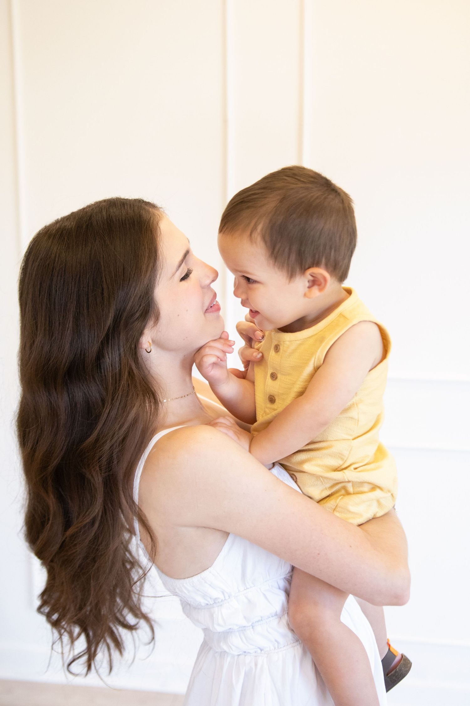 Mother smiling with her baby in her arms in a soft studio setting, captured in a warm motherhood moment.
