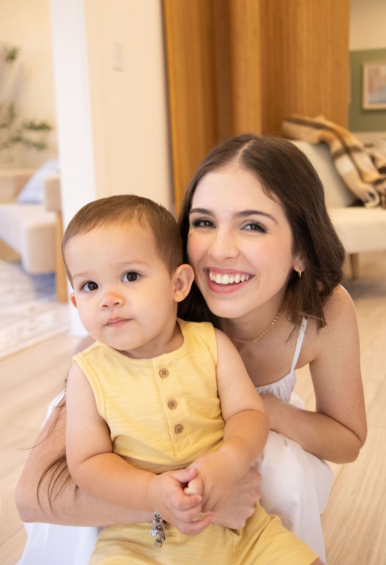 Mother smiling with her baby in a soft studio setting, captured in a warm motherhood moment.