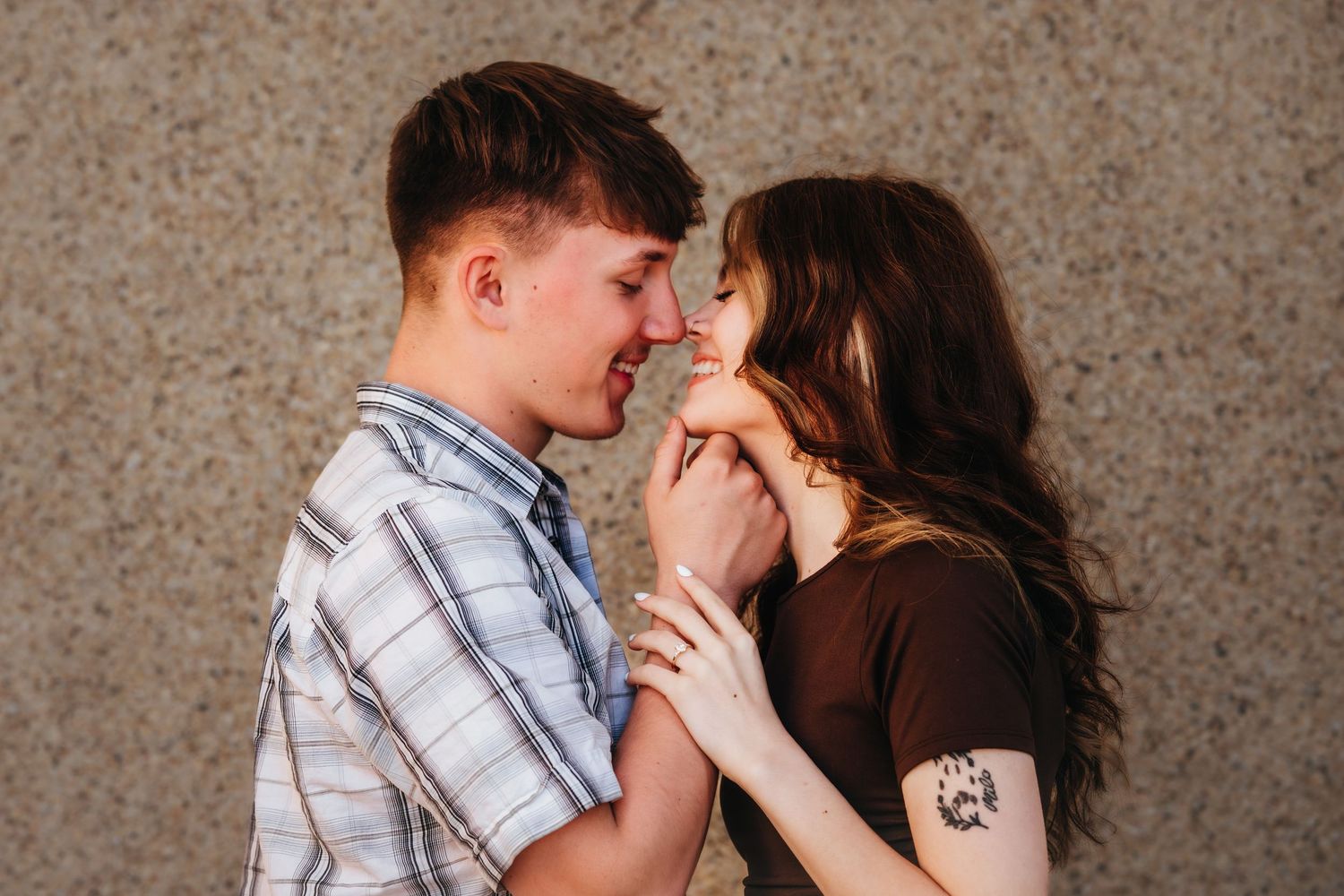 Young couple sharing a romantic moment, almost kissing, standing against a concrete wall outdoors.