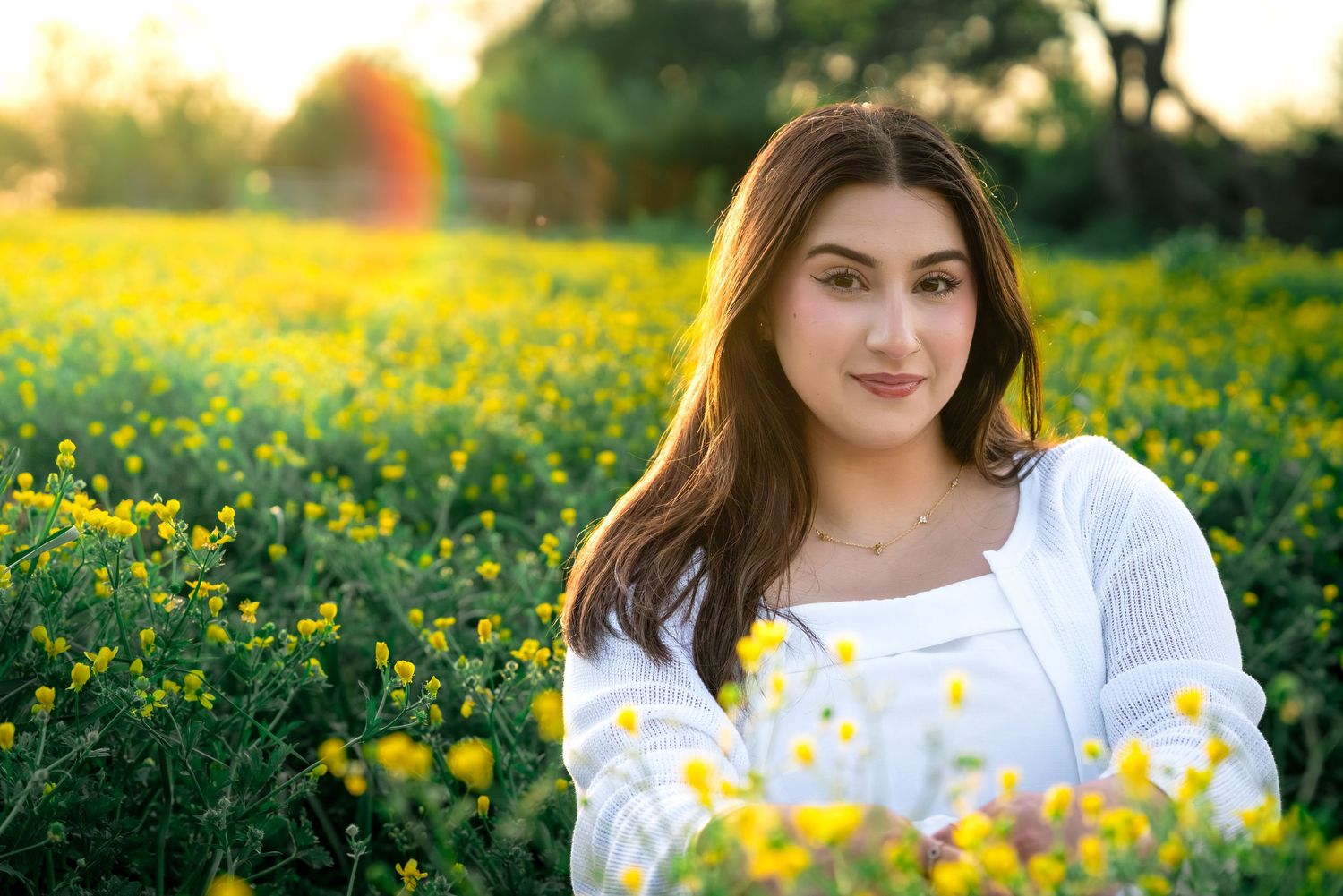 Young woman in white top sitting in a vibrant yellow wildflower field during golden hour sunset.