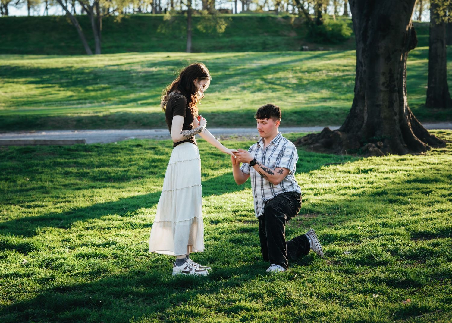 Man presenting engagement ring to woman on bended knee during outdoor park proposal.