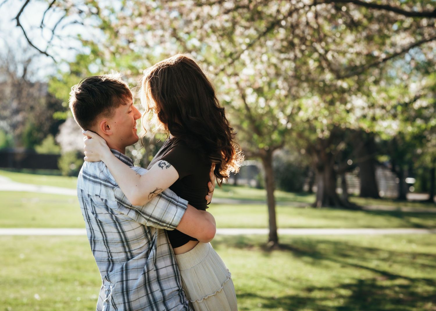 Couple embracing and almost kissing under blooming spring trees in a lush green park on a sunny day.