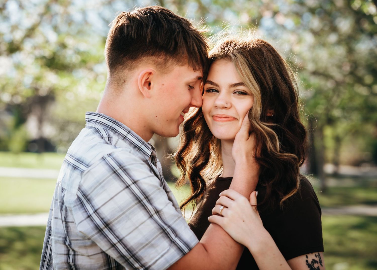 Young couple sharing a tender moment in a blooming park, the man gently touching the woman's face as she smiles.