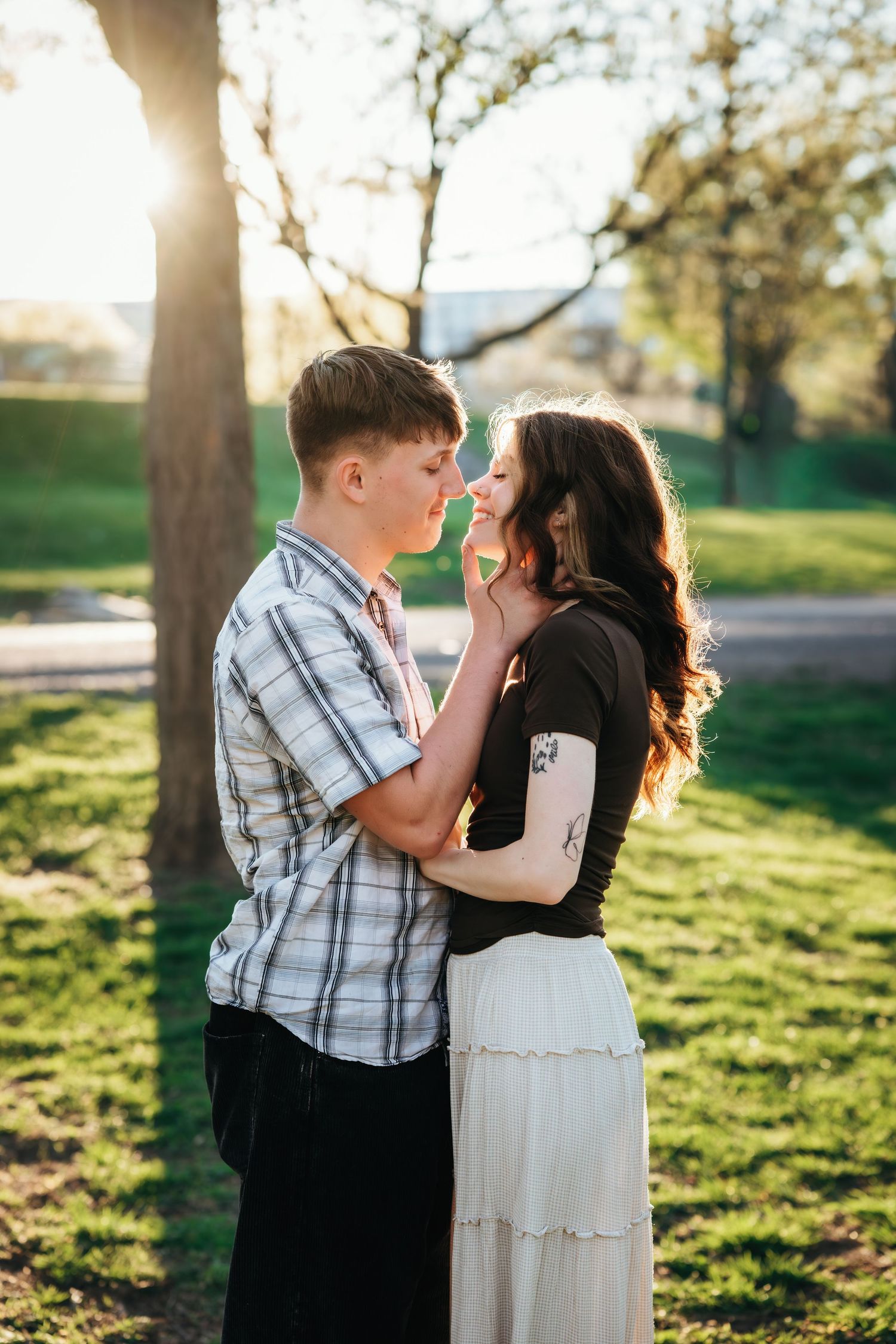 Young couple sharing romantic moment almost kissing in sunny park with golden backlight through trees.