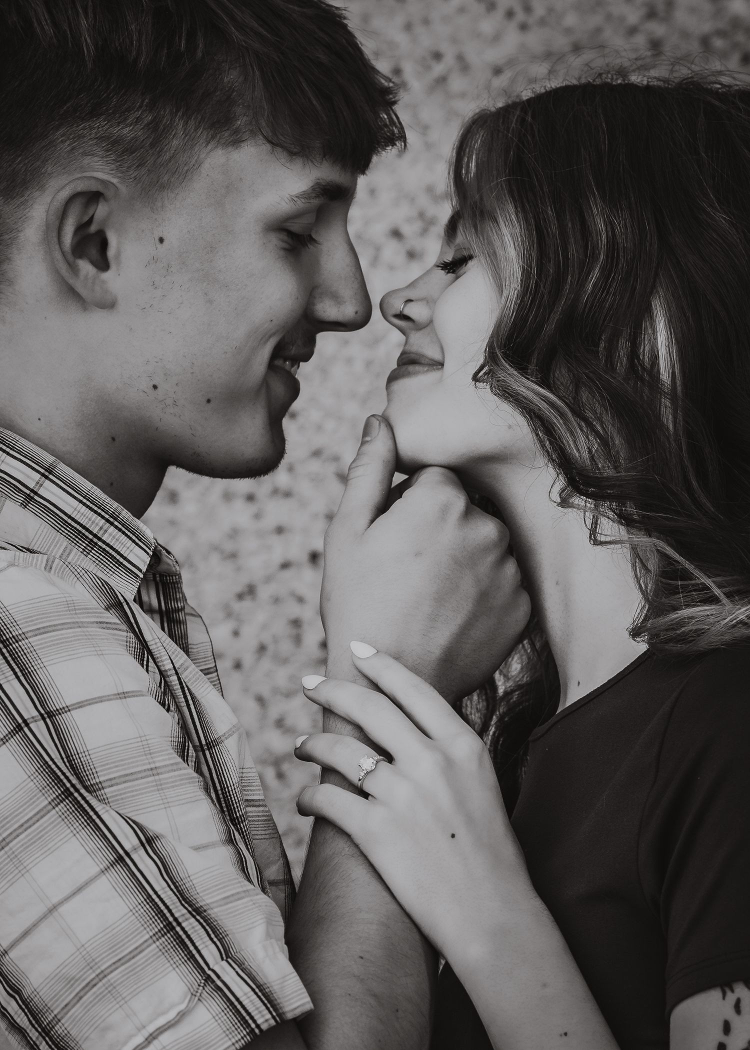 Black and white photo of a young couple sharing a tender romantic moment, faces close together, hands intertwined.