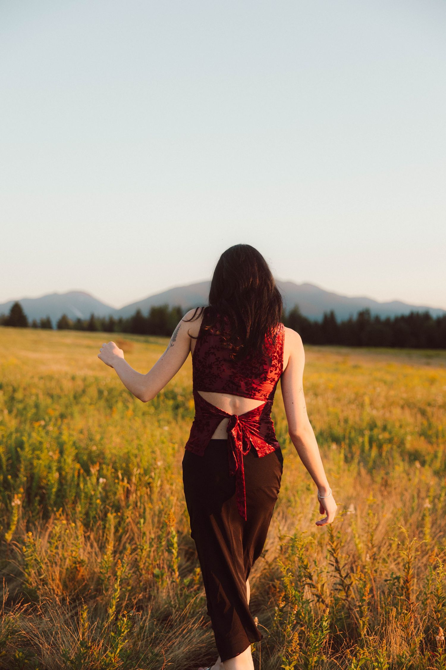 Woman in a red and black dress walking through a wildflower field at sunset.
