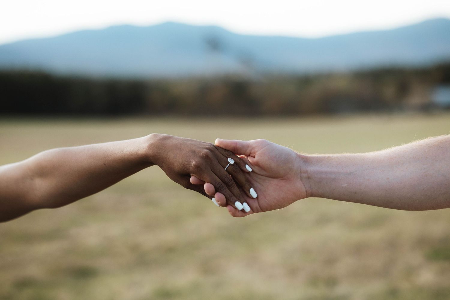Two hands of different skin tones gently clasping together outdoors, symbolizing unity and diversity.
