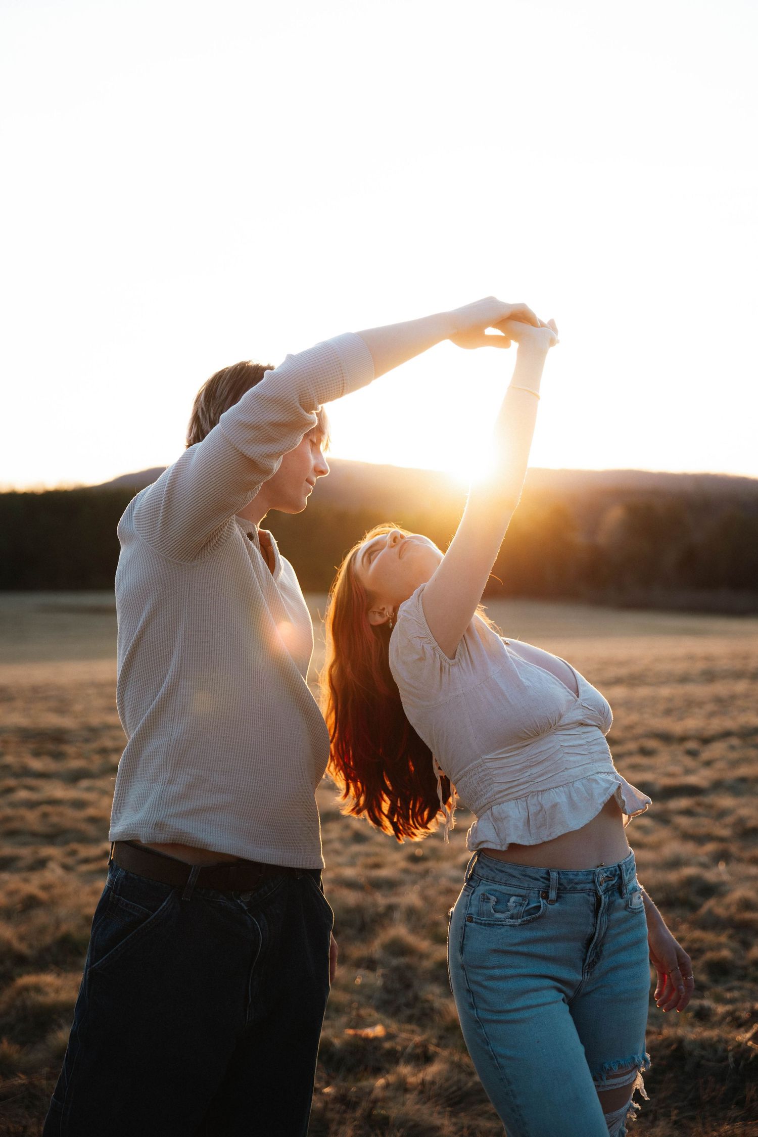 Couple dancing and spinning together in an open field bathed in warm golden sunset light.