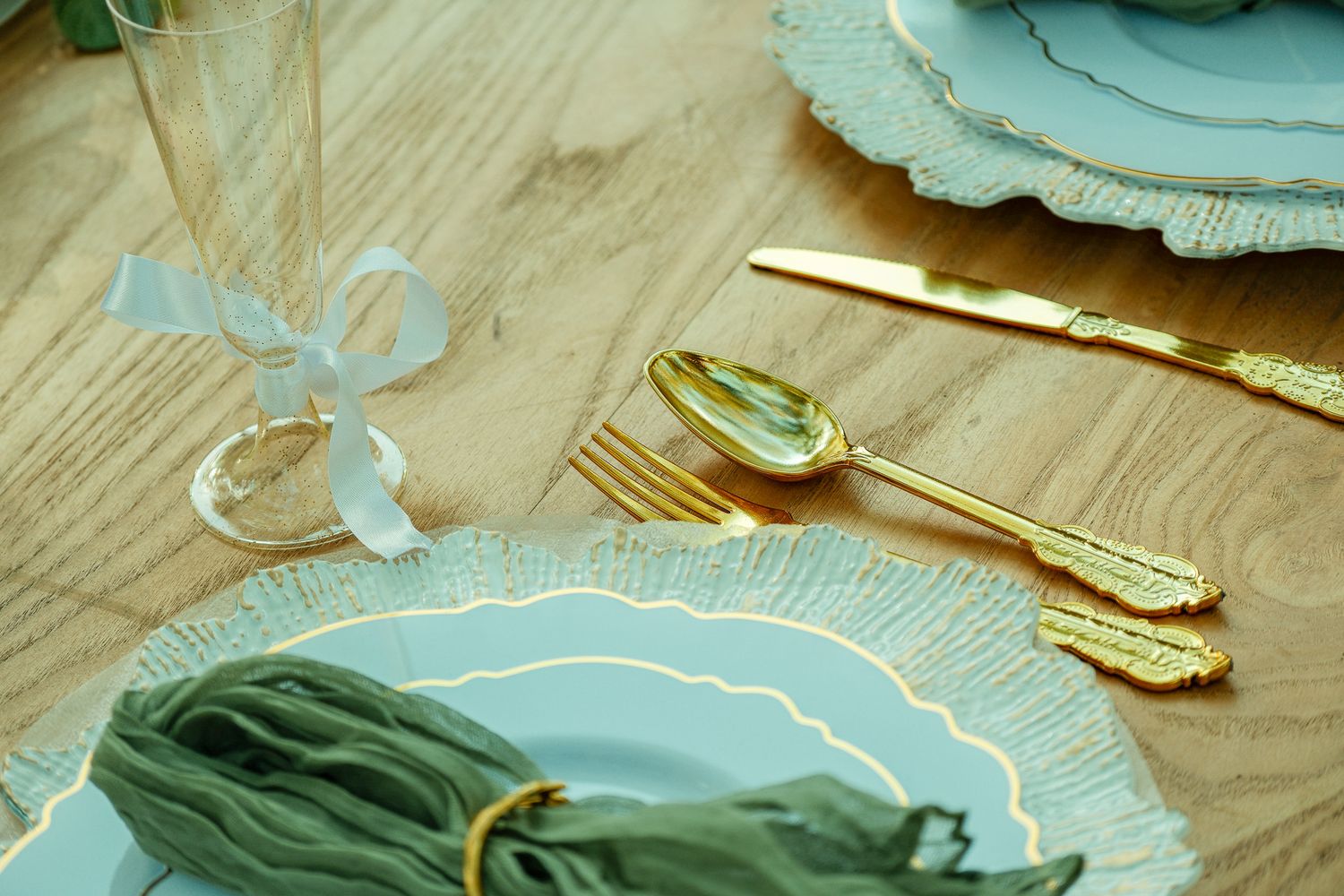 Elegant wedding table setting with gold cutlery, mint green plates, and crystal champagne flute.