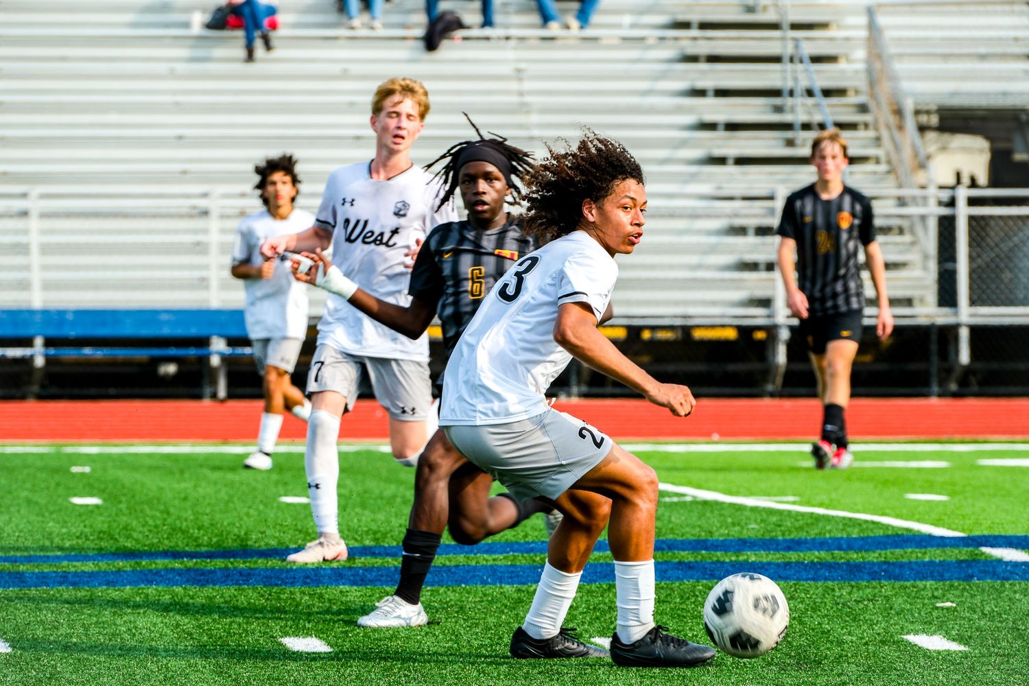 Two soccer players from opposing teams competing for ball control during a match on a blue turf field.