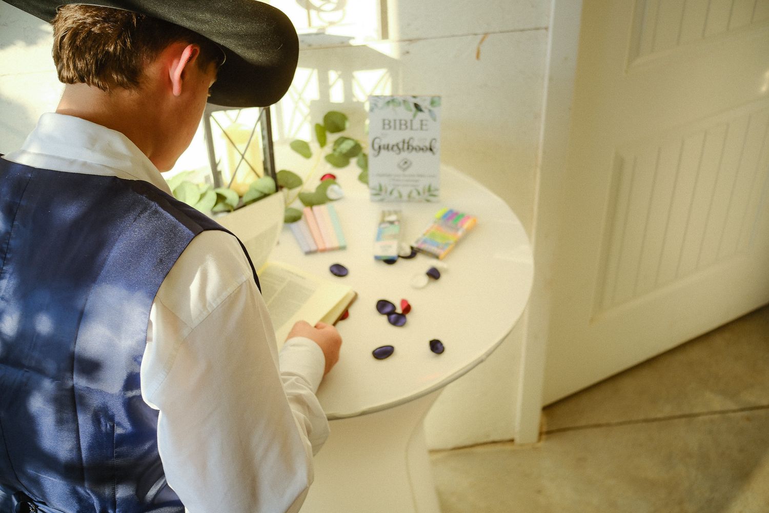Guest signing wedding guestbook at white cocktail table with decorative stones and stationery.