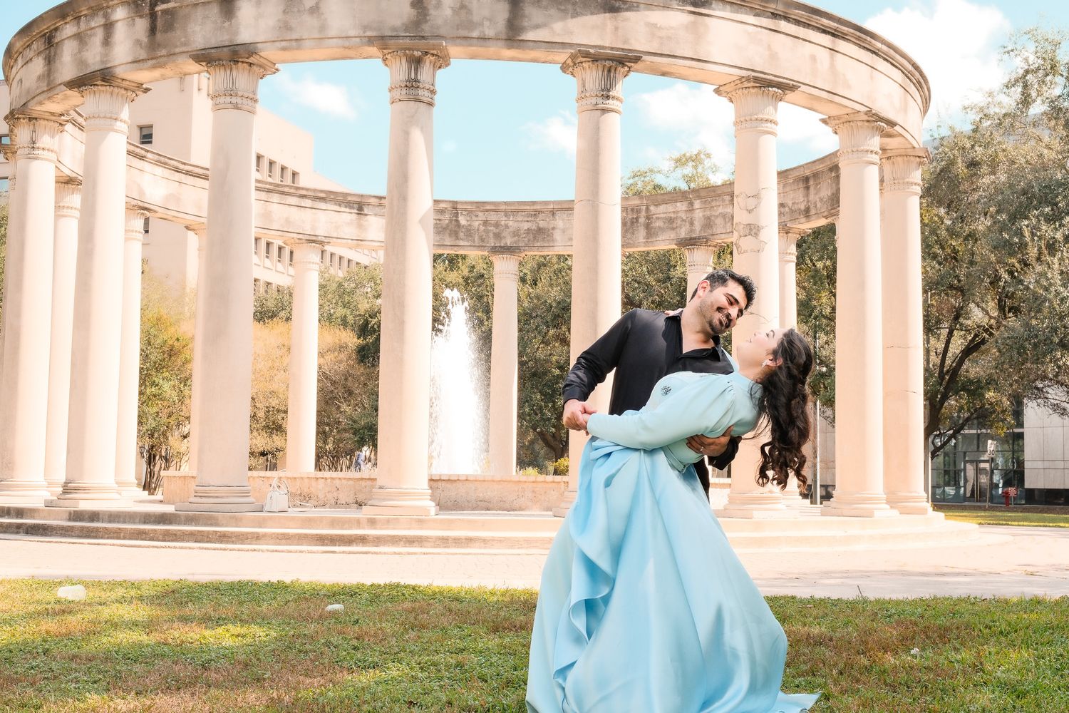 Couple dancing and dipping in front of a classical columned rotunda with fountain.