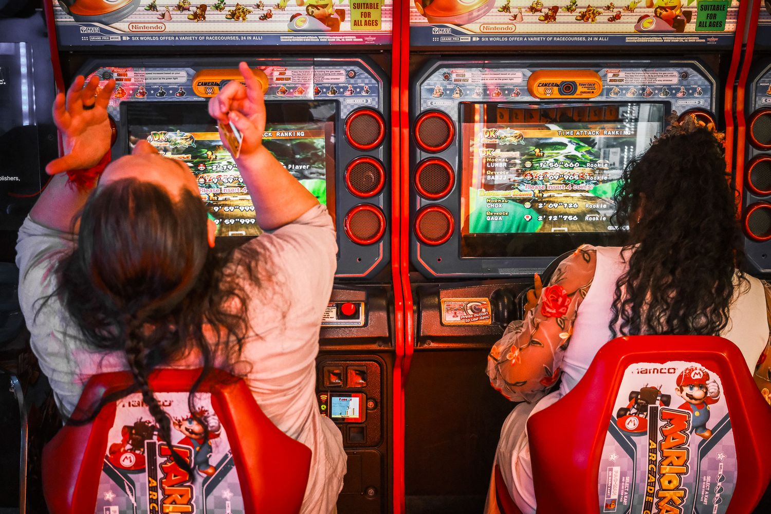 Two women playing arcade games at colorful red gaming machines in an entertainment center.