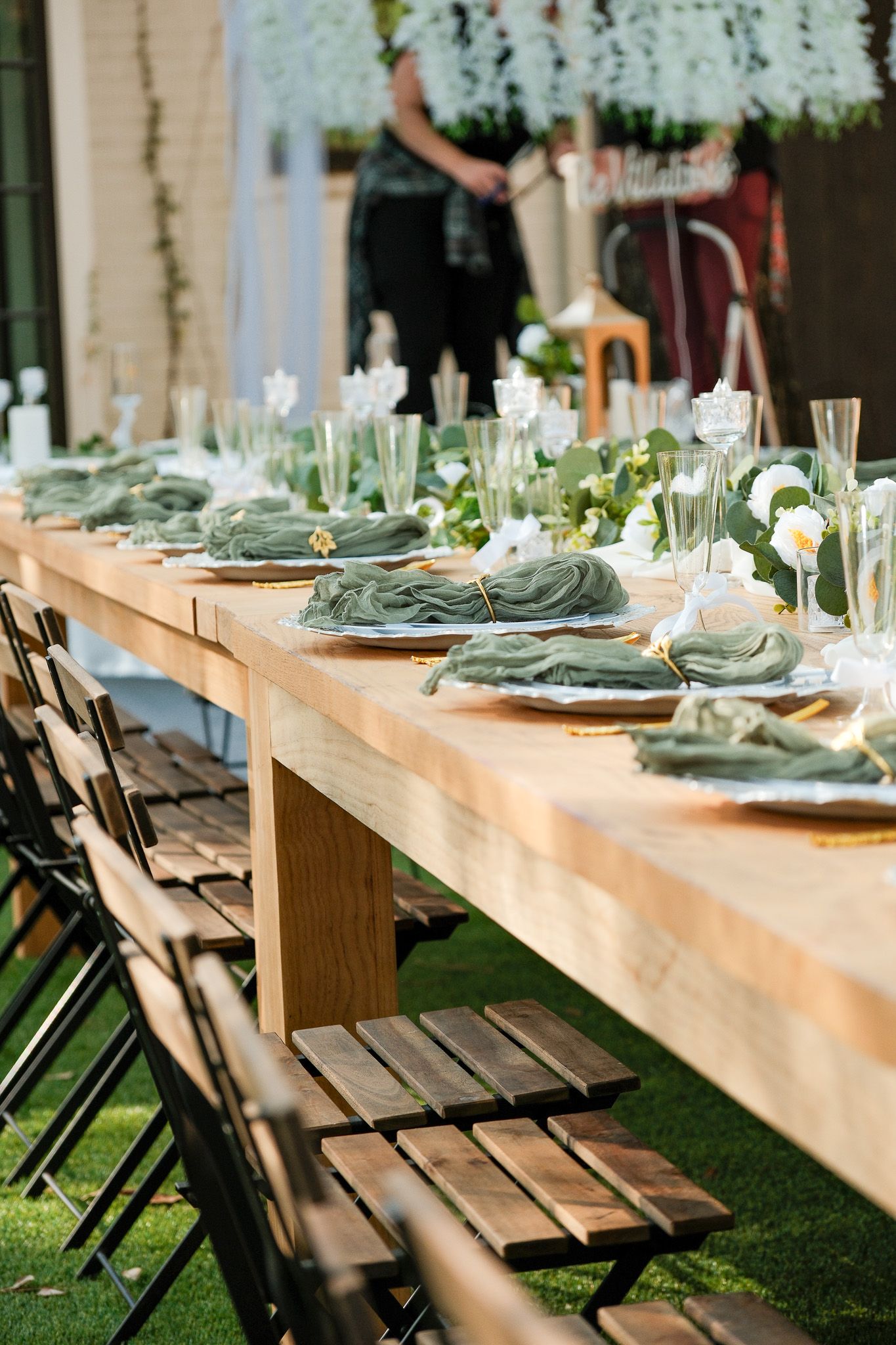Elegant outdoor wedding reception table set with sage green napkins and white florals.