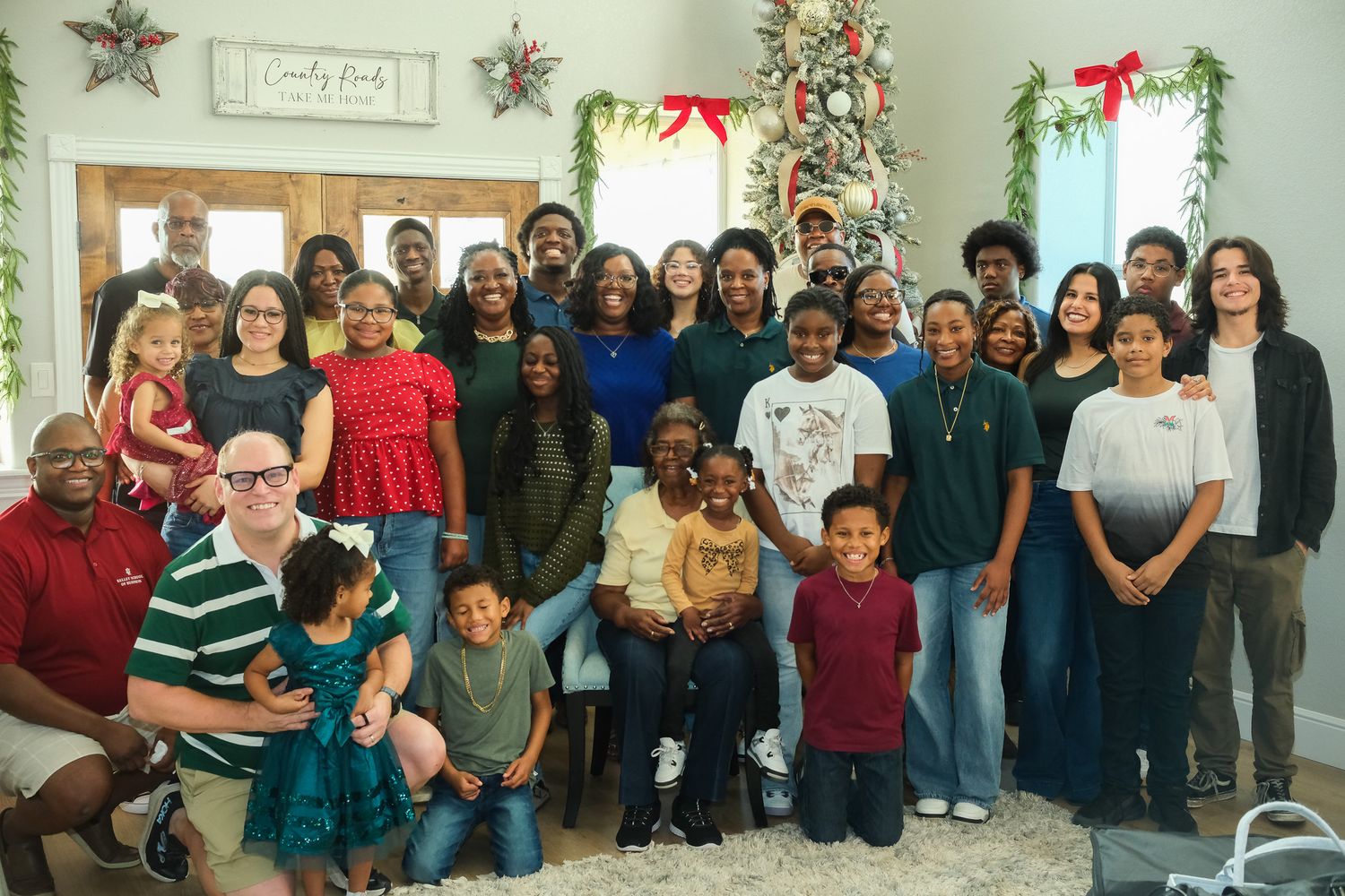 Large multigenerational family group photo gathered indoors near a decorated Christmas tree.